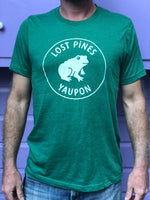 Green shirt with white Lost Pines Yaupon tea logo. Frog with the words Lost Pines above and Yaupon below.